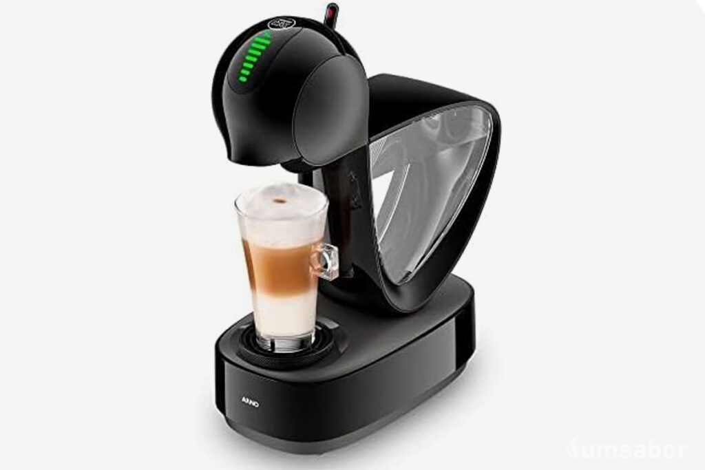 A imagem contém a cafeteira de cápsula dolce gusto infinissima â esquerda com um copo com bebida a base de leite sendo preparada nela. o restante do fundo é branco.