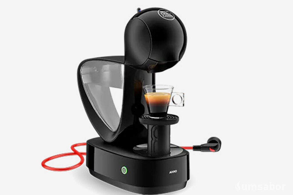 A imagem contém a cafeteira de cápsula dolce gusto infinissima ao centro com uma xícara de café com bebida sendo preparada nela. o restante do fundo é branco.