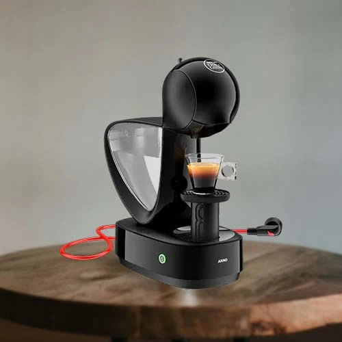 A imagem é composta por uma mesa de madeira e em cima dessa mesa há uma cafeteira dolce gusto Infinissima de cor preta com um copo com café dentro e o cabo de energia da máquina é de cor vermelha