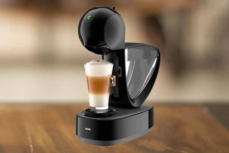 Dolce Gusto Infinissima é boa? Análise Completa 24 A imagem é composta pela cafeteira de cápsula Dolce Gusto Infinissima de cor preta ao centro. Além disso, nessa cafeteira tem um copo com bebida a base de leite dentro. Essa cafeteira está em cima de uma mesa de madeira e o fundo restante está desfocado.